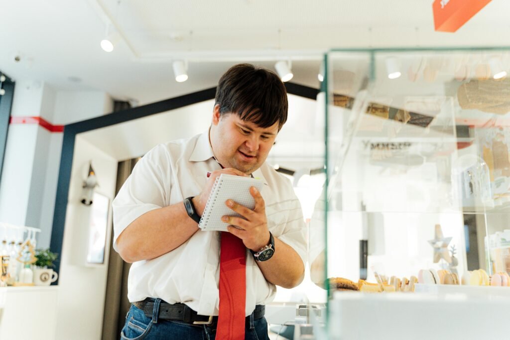 A man in an office environment, writing notes on a notepad, surrounded by work-related items.